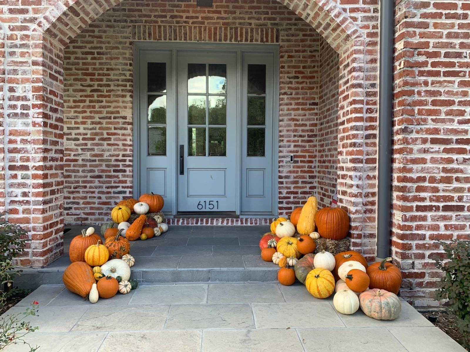 Light blue door framed by red brick, decorated with clusters of colorful pumpkins and gourds.