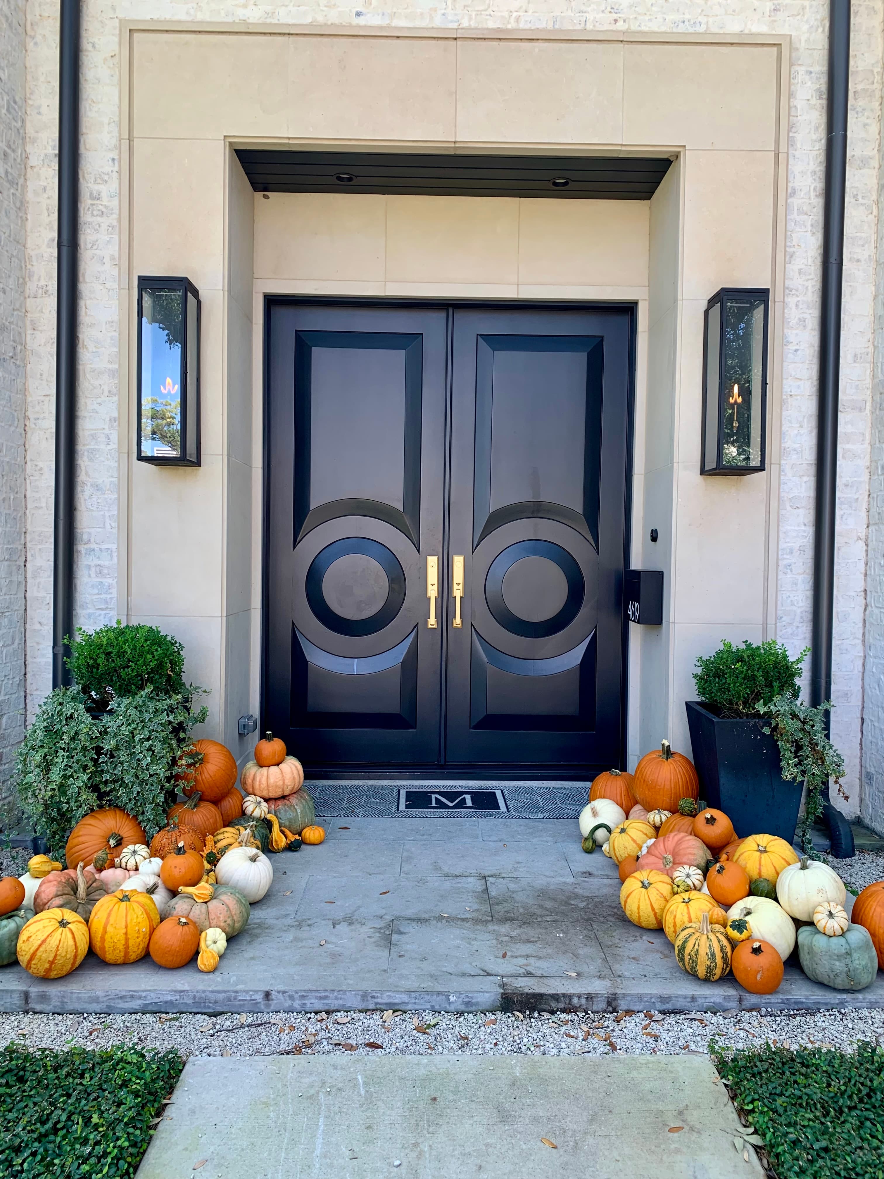 Modern black double doors framed by a festive display of colorful pumpkins and gourds.
