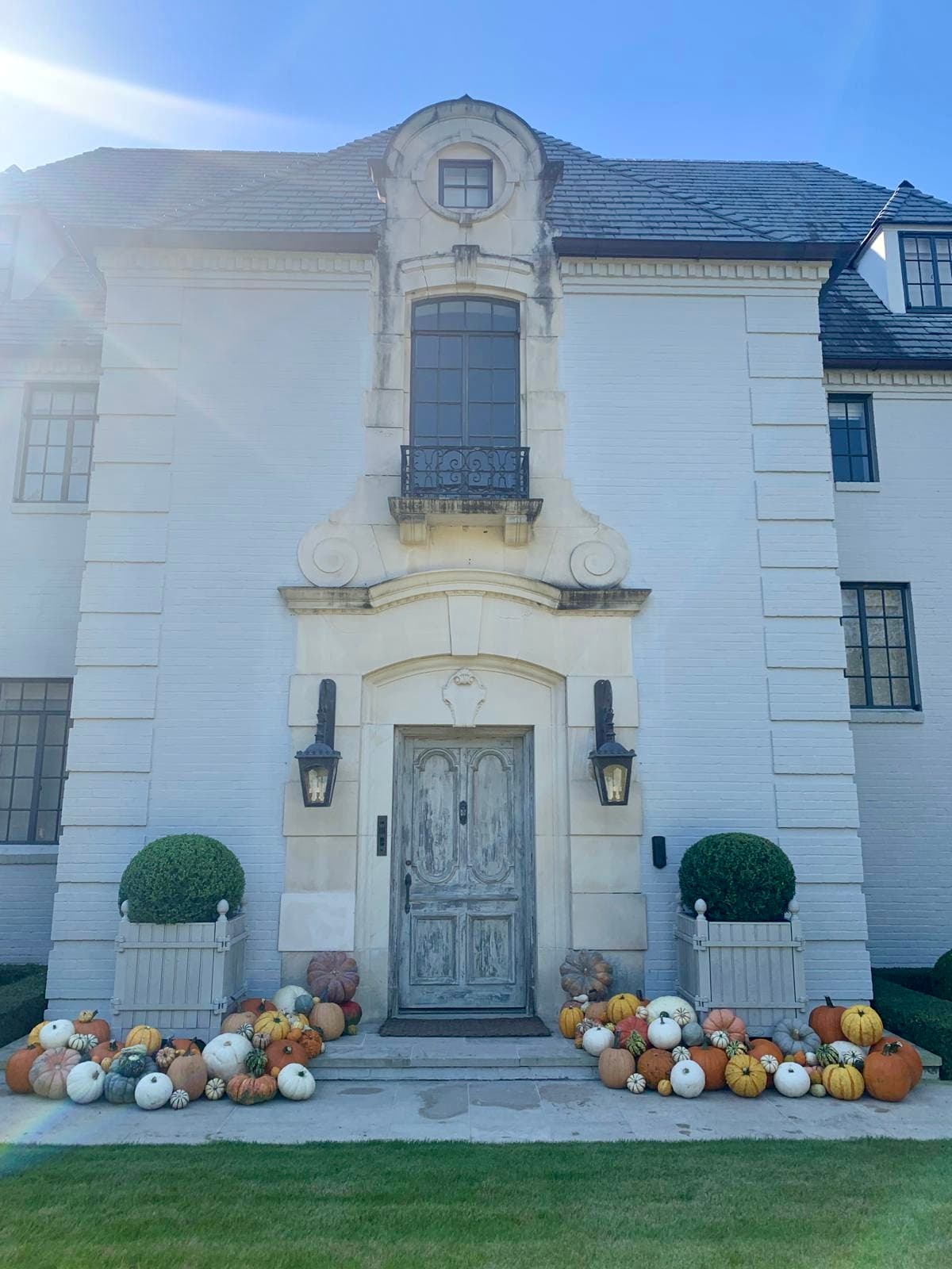 Ornate white house entrance decorated for autumn with a large collection of colorful pumpkins.