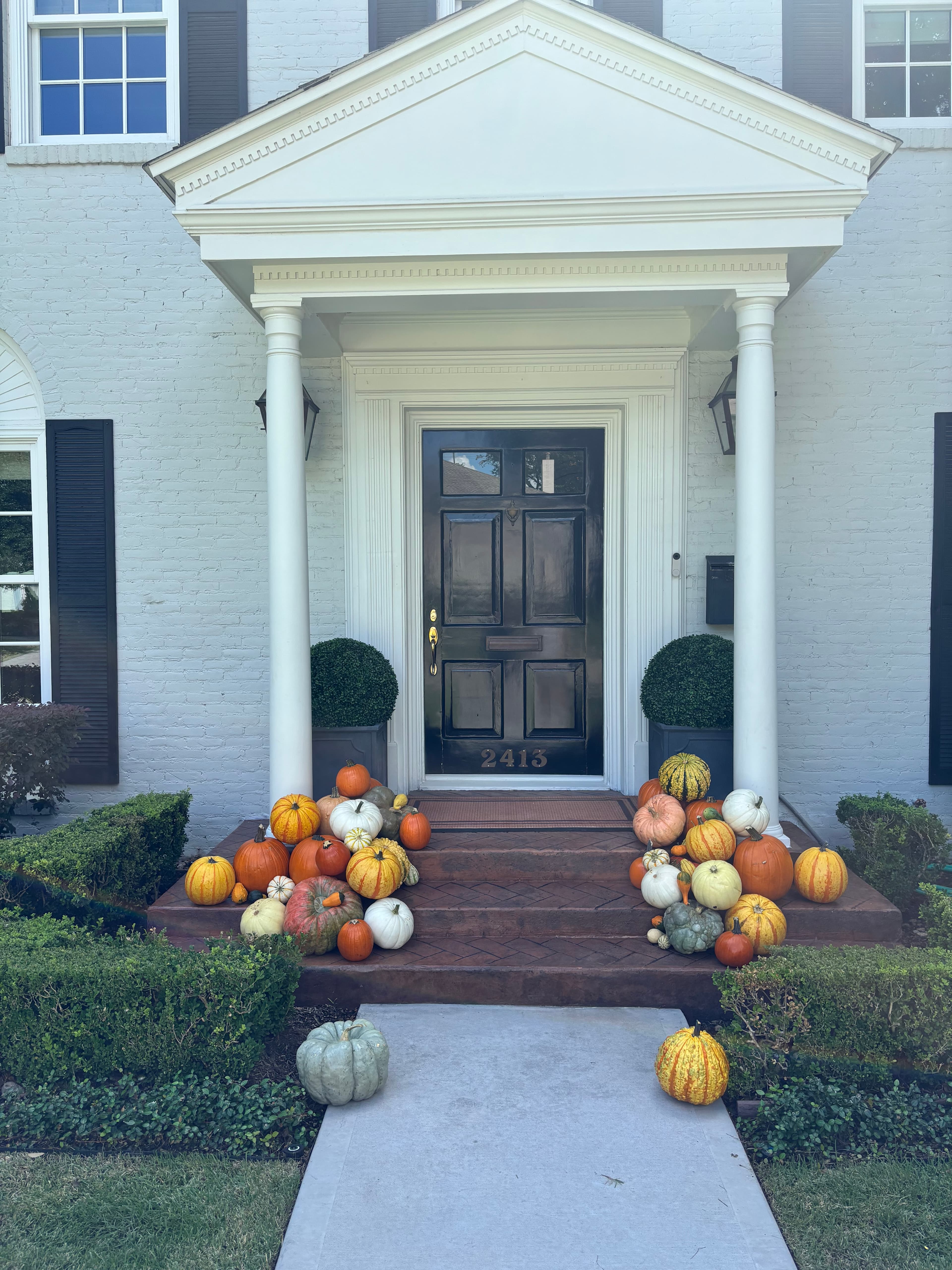 Colorful pumpkins and gourds decorate the steps of a white brick house with black door.