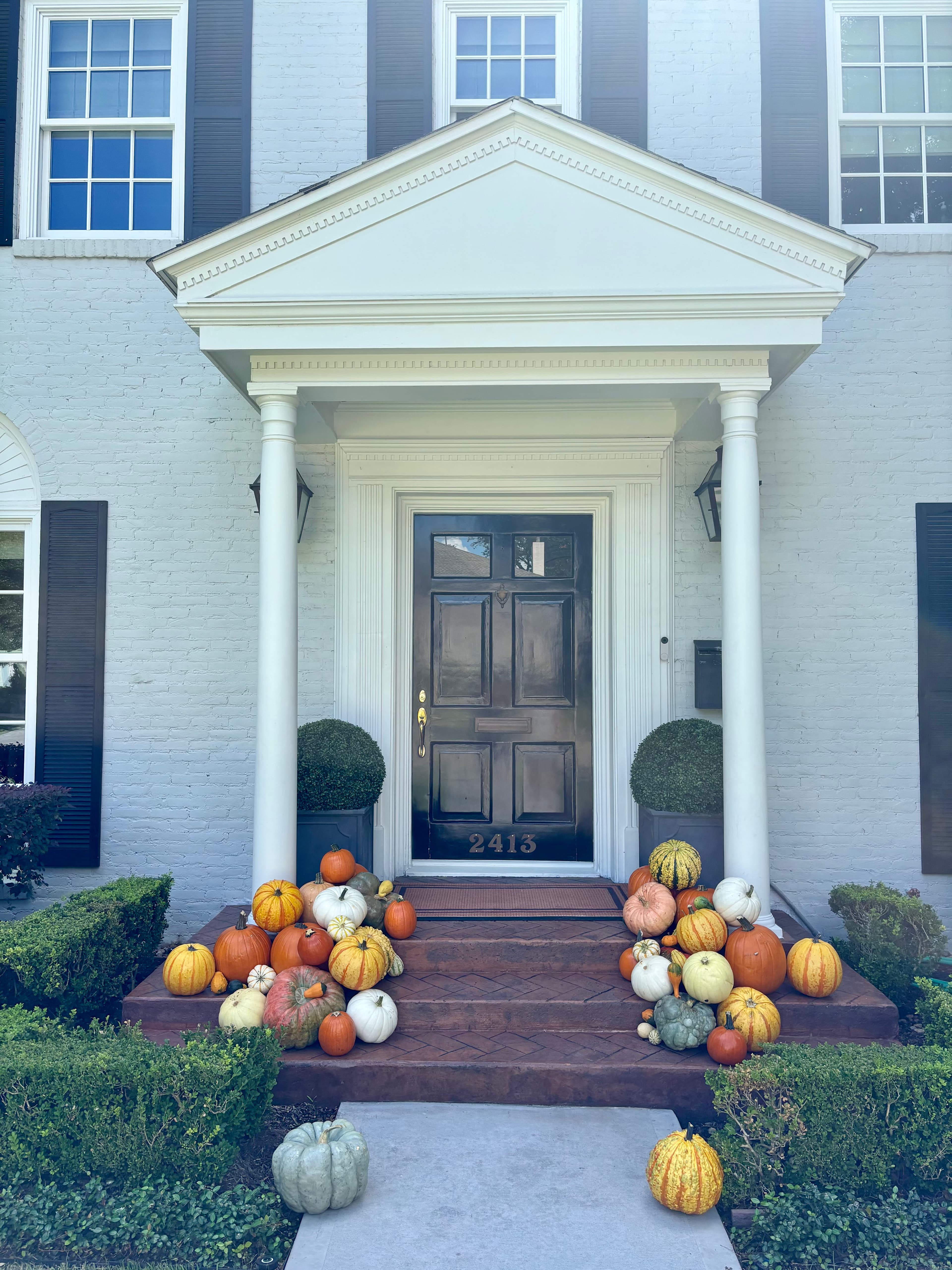 Colorful pumpkins and gourds decorate the steps of a white house with a black door.